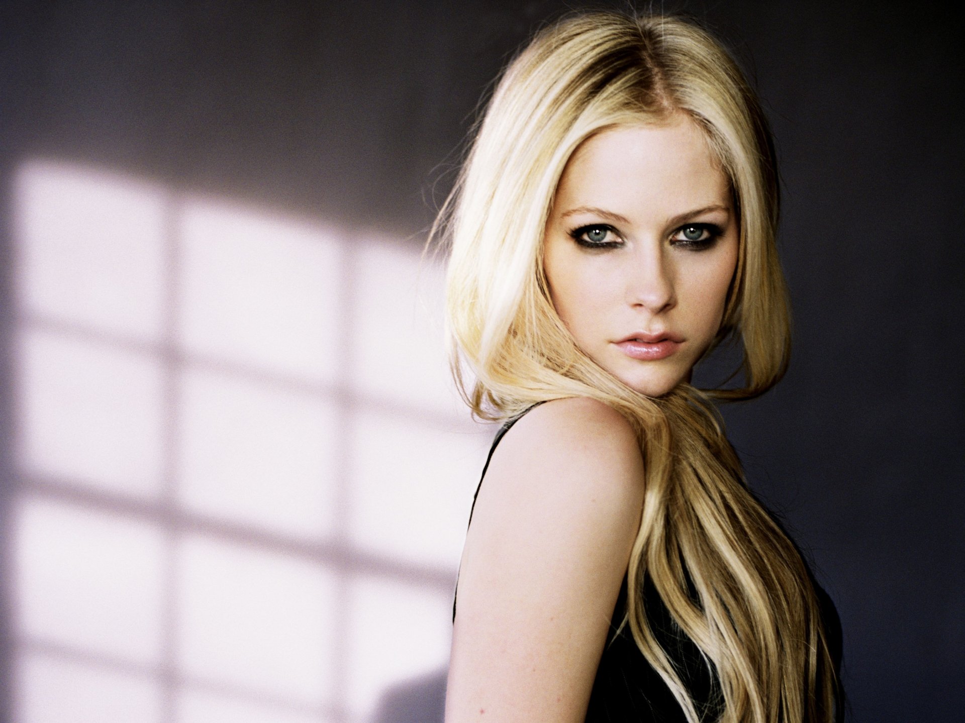 A stunning HD desktop wallpaper featuring Avril Lavigne, showcasing her signature blonde hair and striking makeup against a soft, shadowy background.