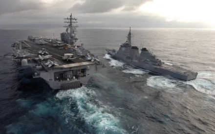 Aerial view of the USS Ronald Reagan (CVN-76) aircraft carrier navigating through ocean waters alongside a military escort vessel. Military strength meets maritime power in this striking image.