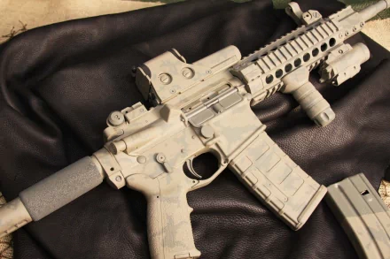 Close-up 4K Ultra HD image of a man-made assault rifle with attachments resting on a dark surface, showcasing intricate details and textures.