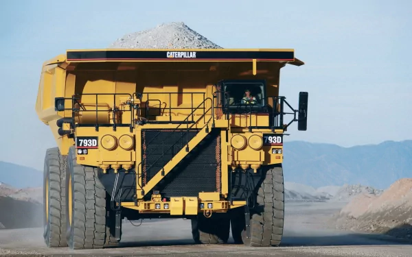 A Caterpillar Inc. vehicle, the massive 793D dump truck, drives on a rugged road, transporting a load of gravel against a backdrop of mountains. High-definition desktop wallpaper.