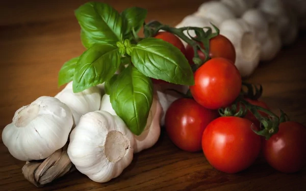 HD desktop wallpaper featuring fresh vegetables including garlic bulbs, ripe red tomatoes on the vine, and vibrant green basil leaves, displayed on a wooden surface.