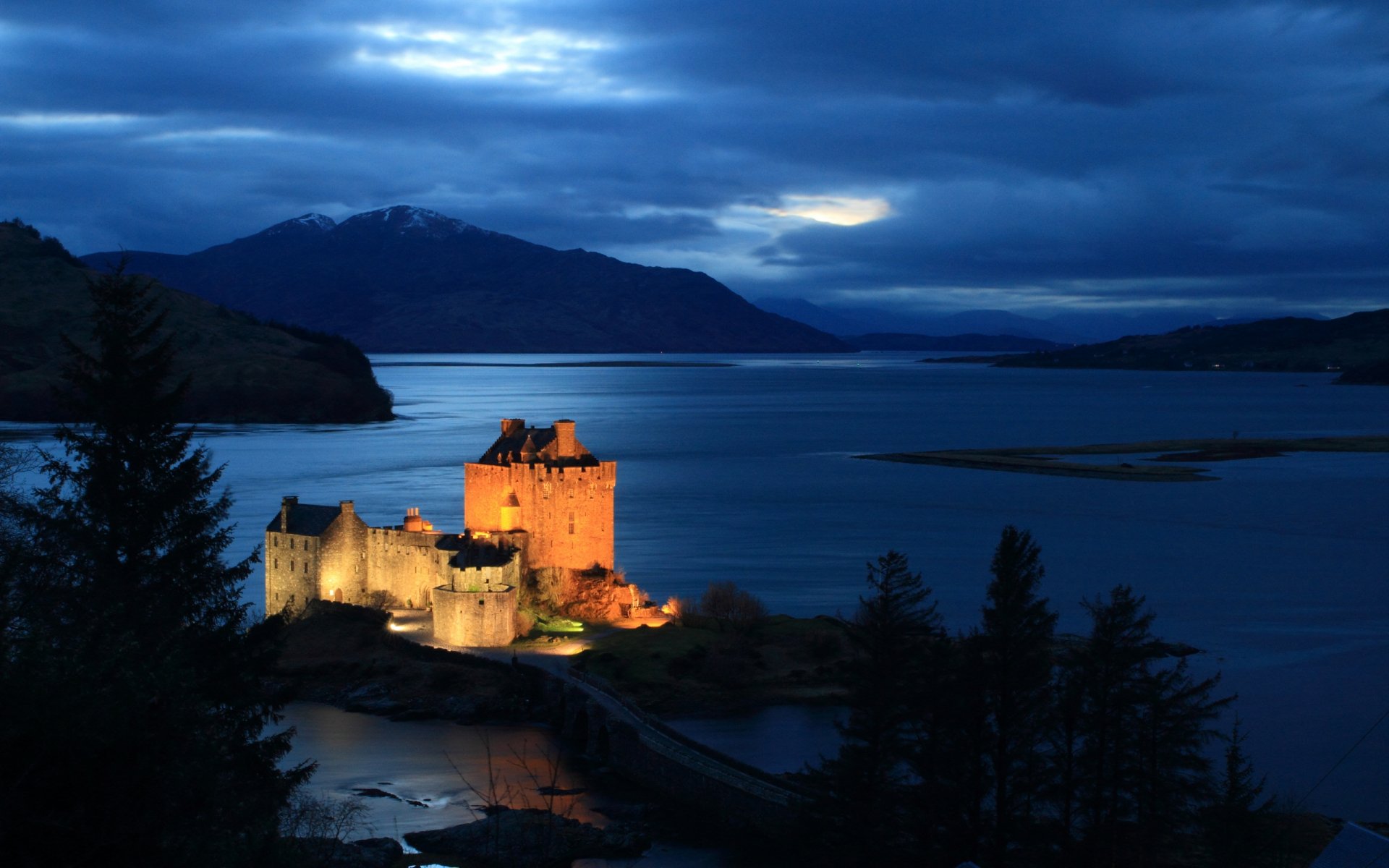A stunning view of Eilean Donan Castle illuminated at dusk, surrounded by tranquil waters and silhouetted by mountains, making a captivating HD desktop wallpaper.