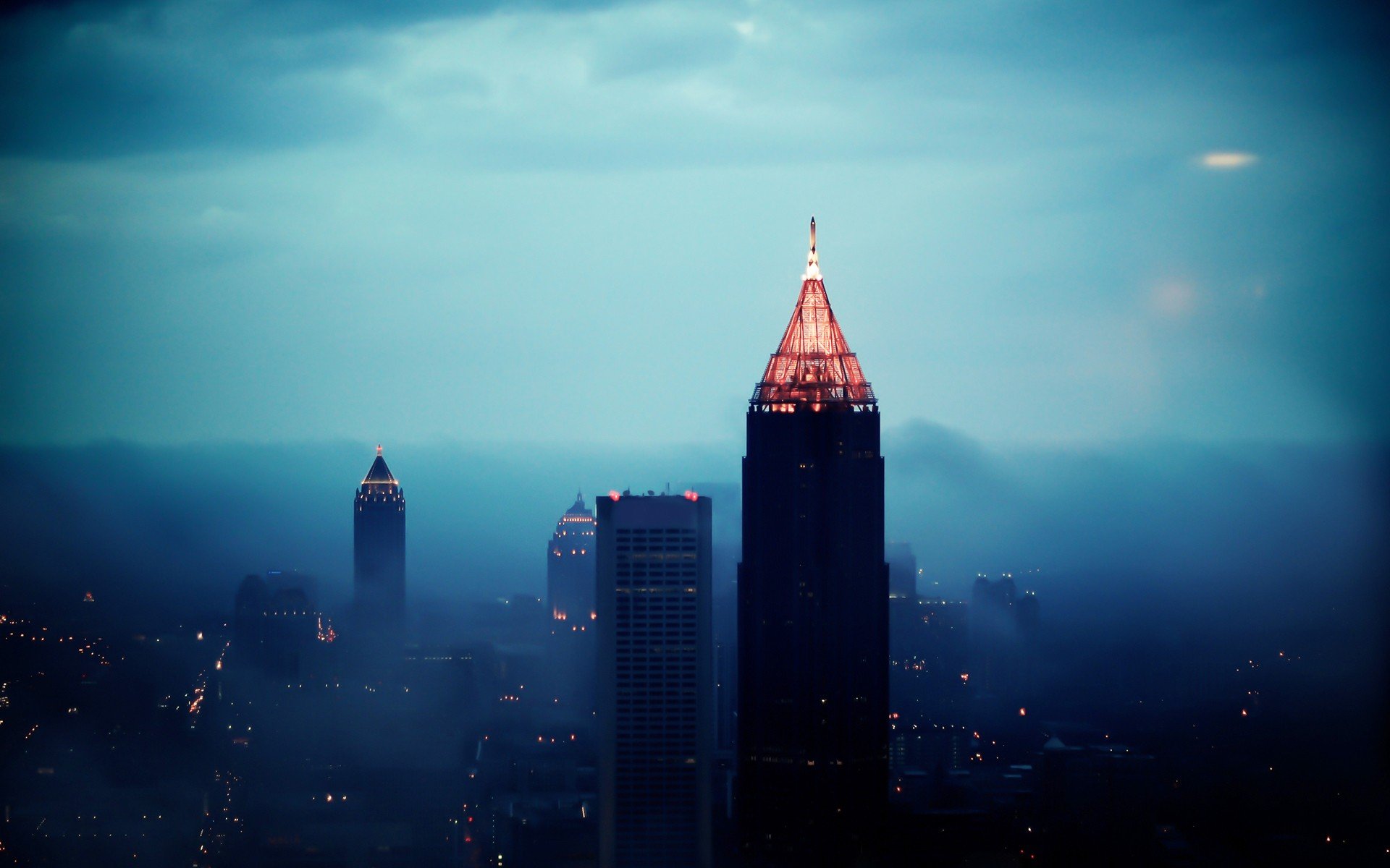 HD PC desktop wallpaper: moody Atlanta skyline at dusk, man-made skyscrapers rising through low fog, a central tower crowned in warm light.