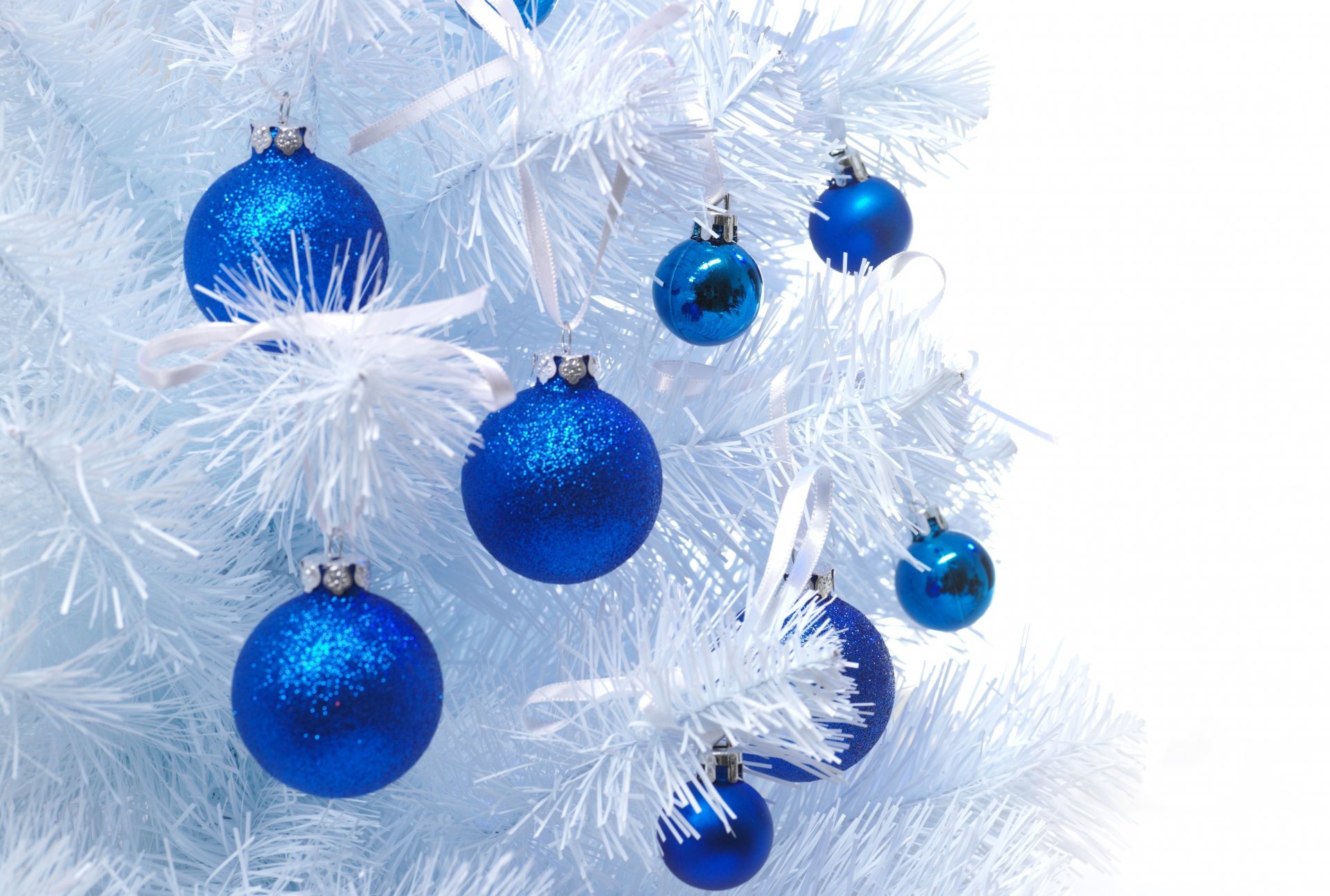 A close-up of blue Christmas ornaments hanging on a white artificial tree, creating a festive holiday atmosphere. This HD wallpaper adds a cheerful touch to any desktop background.