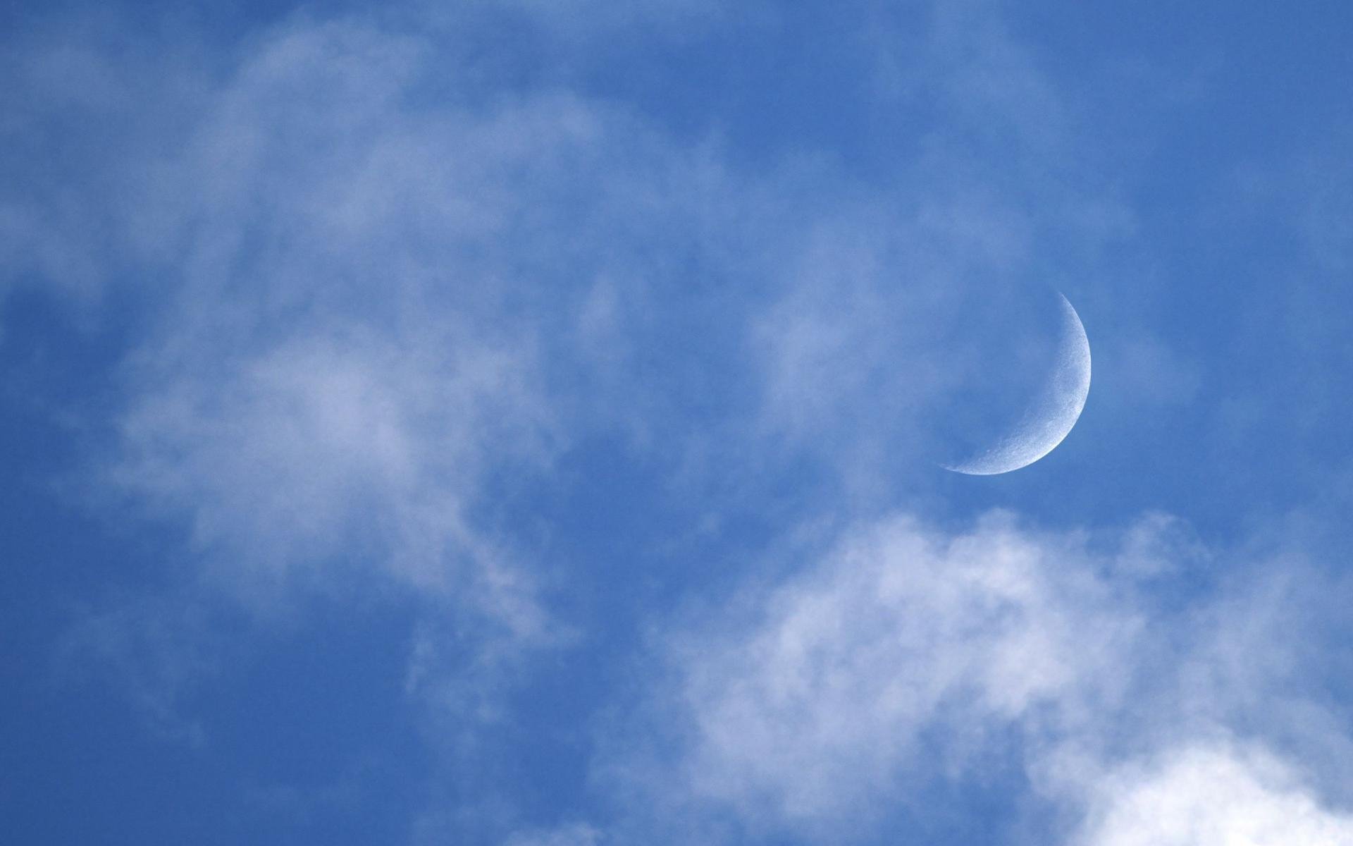 HD PC desktop wallpaper showing a crescent moon peeking through wispy clouds in a clear blue sky — a serene nature scene.