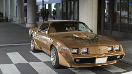 HD PC desktop wallpaper featuring a classic gold Pontiac Trans Am parked on a city street under modern architecture.