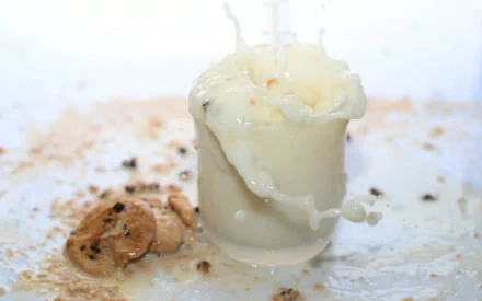 HD desktop wallpaper showcasing a splash of milk in a glass, surrounded by scattered cookies and crumbs.