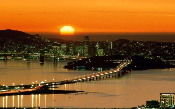2K Quad HD PC wallpaper: San Francisco skyline with man-made Bay Bridge aglow at sunset, city lights reflecting across the calm bay.