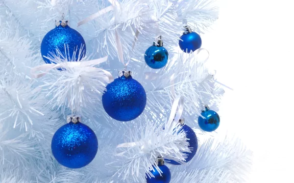 A close-up of blue Christmas ornaments hanging on a white artificial tree, creating a festive holiday atmosphere. This HD wallpaper adds a cheerful touch to any desktop background.