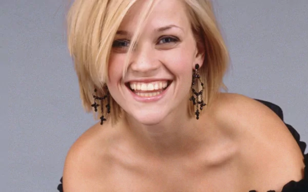 HD desktop wallpaper featuring a smiling Reese Witherspoon with short blonde hair and black cross earrings against a plain gray background.