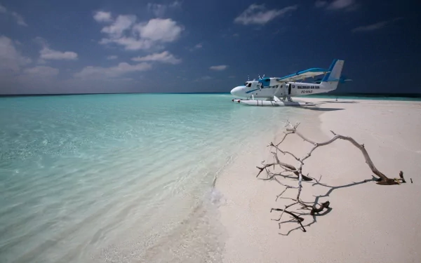 A De Havilland Canada DHC-6 Twin Otter seaplane rests on a pristine, sandy beach beside clear turquoise waters, with a stunning ocean horizon and dramatic sky in the Maldives.