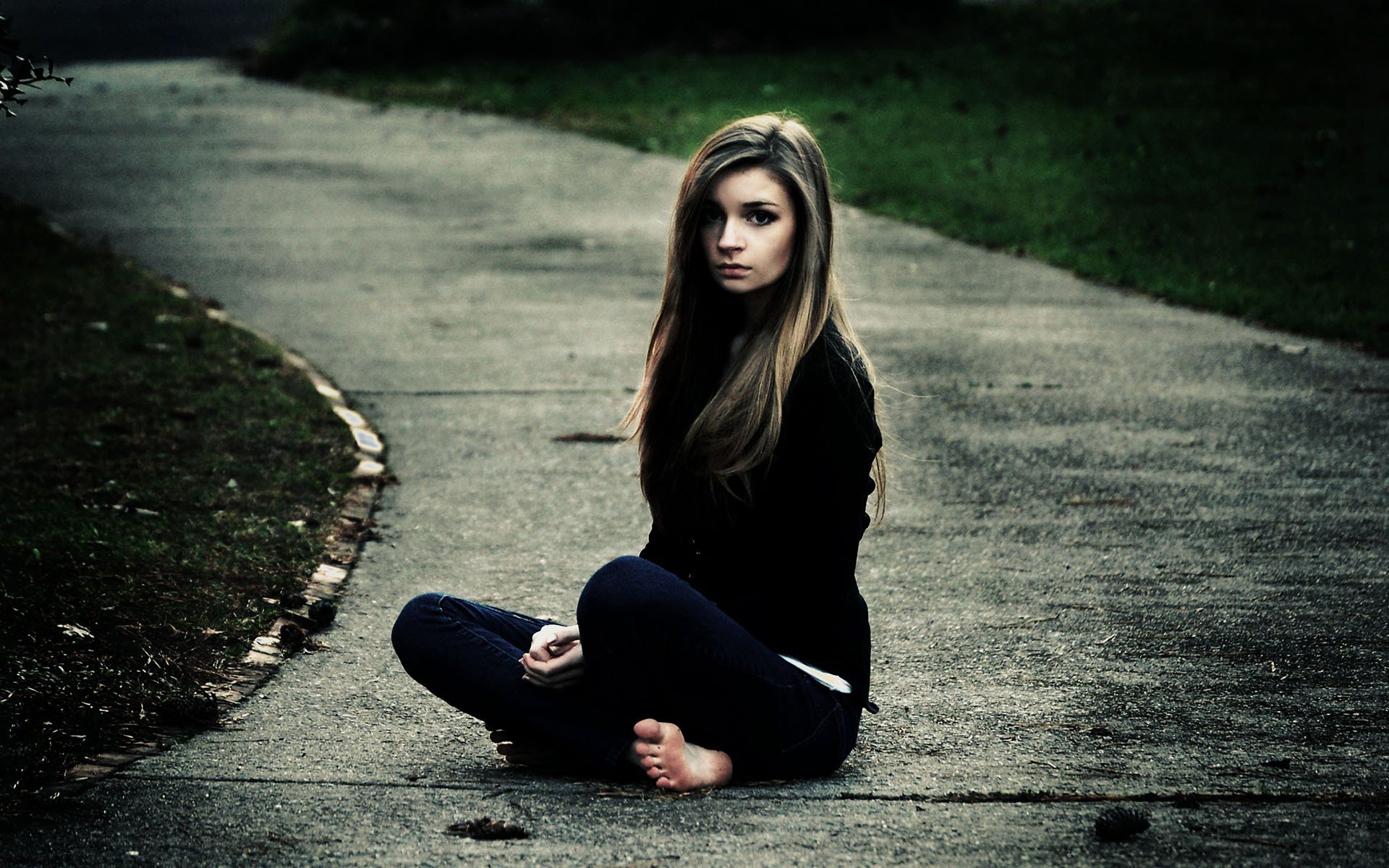 A woman with long hair sits on a pathway, barefoot, wearing black attire. This HD image serves as a striking desktop wallpaper and background.