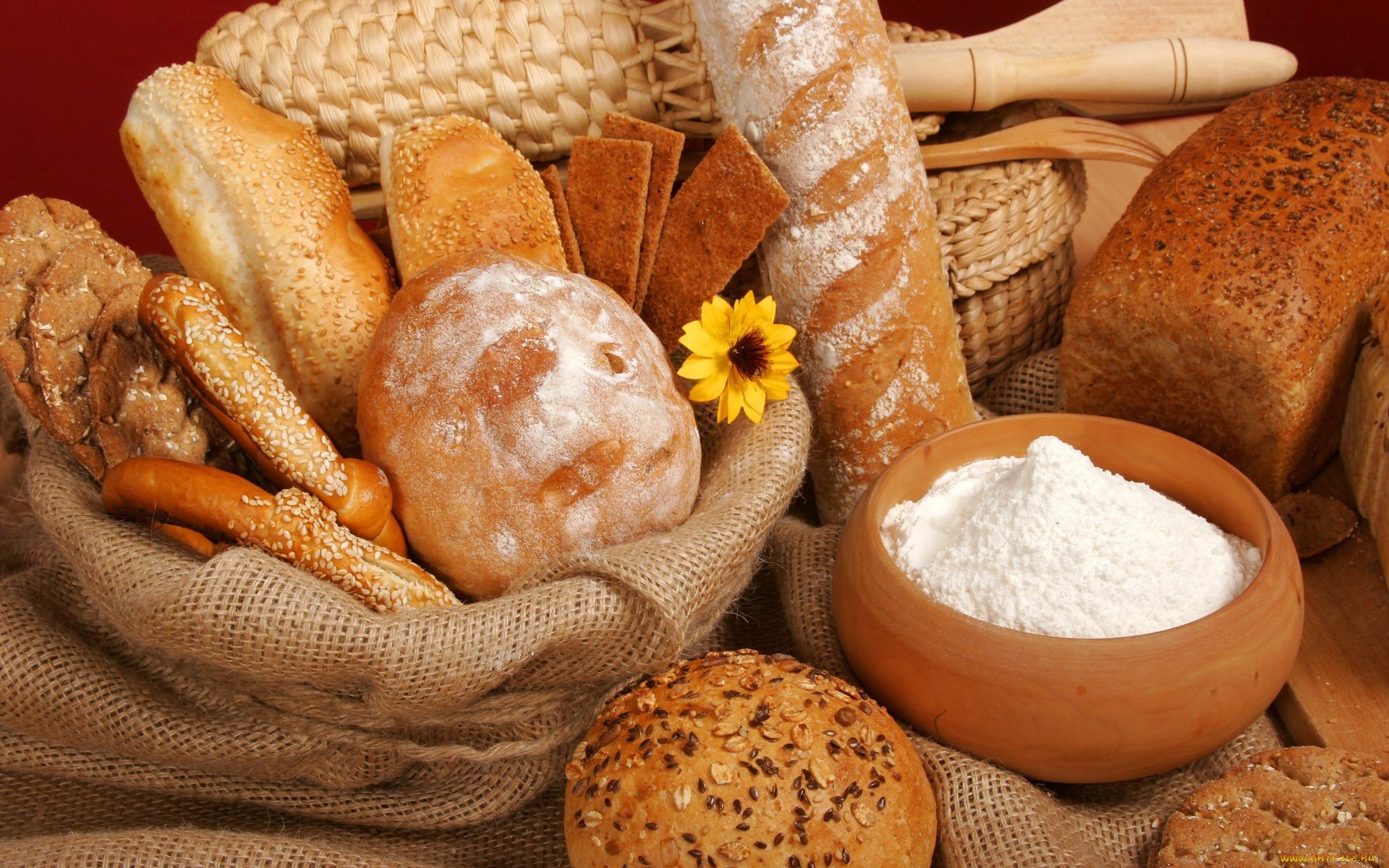 HD desktop wallpaper featuring various breads, a bowl of flour, and baking ingredients arranged on a rustic burlap surface, highlighting food and baking themes.