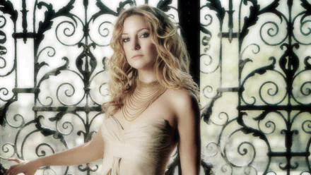 HD desktop wallpaper featuring celebrity Kate Hudson in a soft, elegant pose with flowing blonde hair and a layered necklace against an ornate wrought iron background.