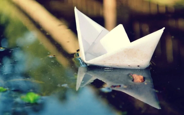 HD desktop wallpaper featuring a close-up of an origami paper boat floating on calm water, highlighting its detailed paper folds and reflection.