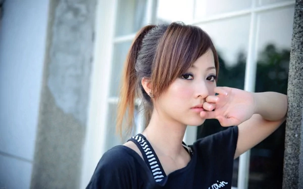 A woman named Mikako Zhang Kaijie poses thoughtfully against a wall, showcasing a blend of elegance and casual style in this HD desktop wallpaper.