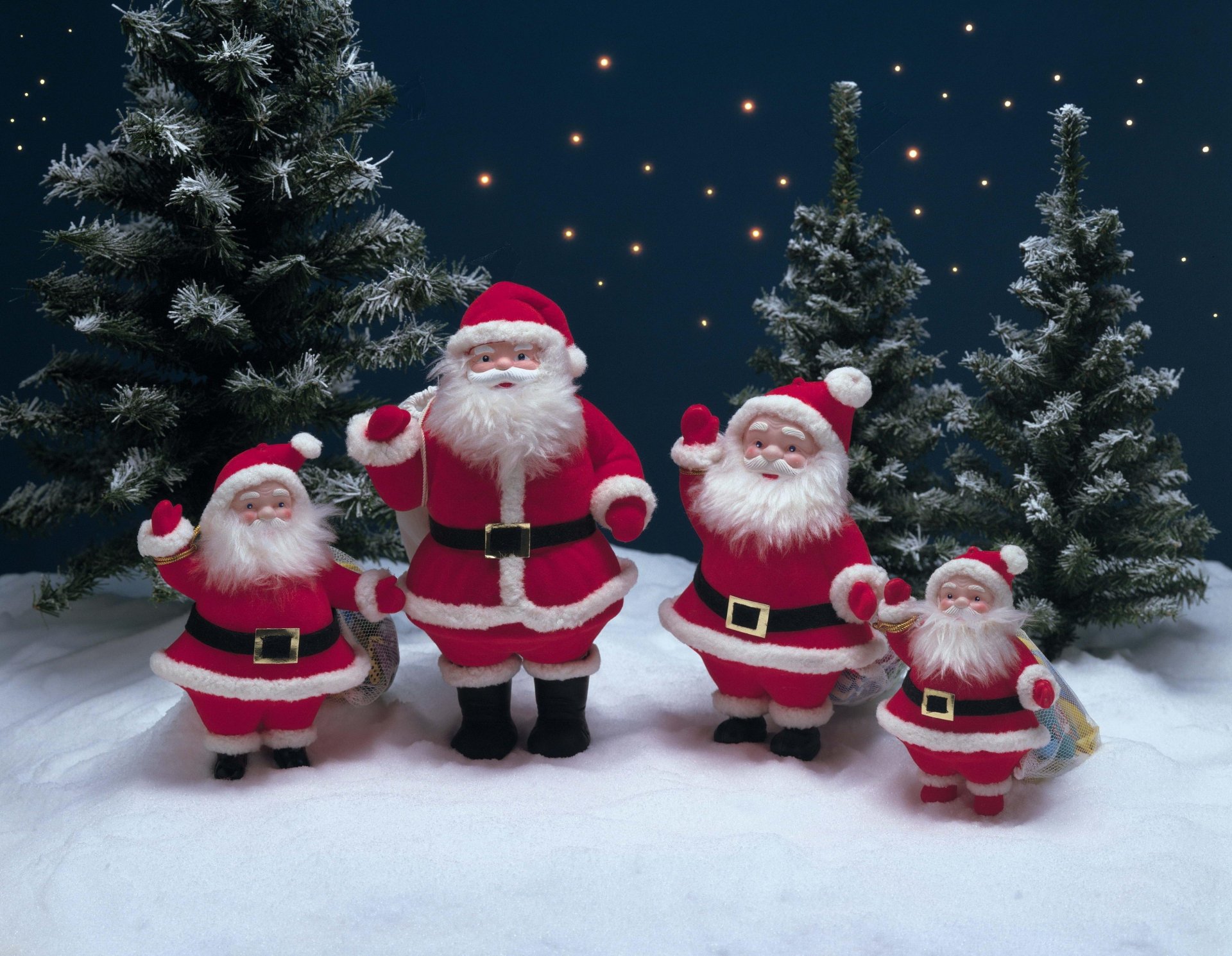 HD desktop wallpaper featuring a snowy scene with four Santa Claus figures waving, surrounded by Christmas trees with stars in the night sky. Holiday charm and festive spirit fill the background.