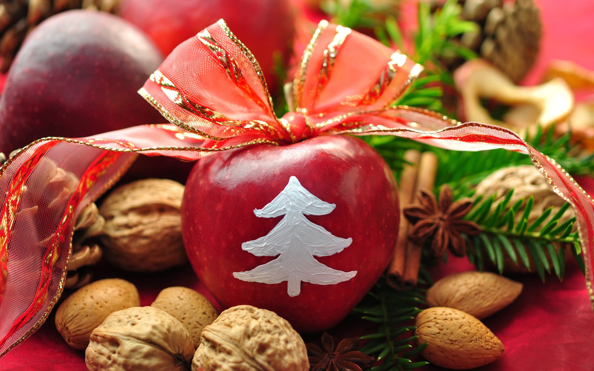 HD Christmas holiday desktop wallpaper featuring a decorated red apple with a white tree, surrounded by nuts and festive greenery.