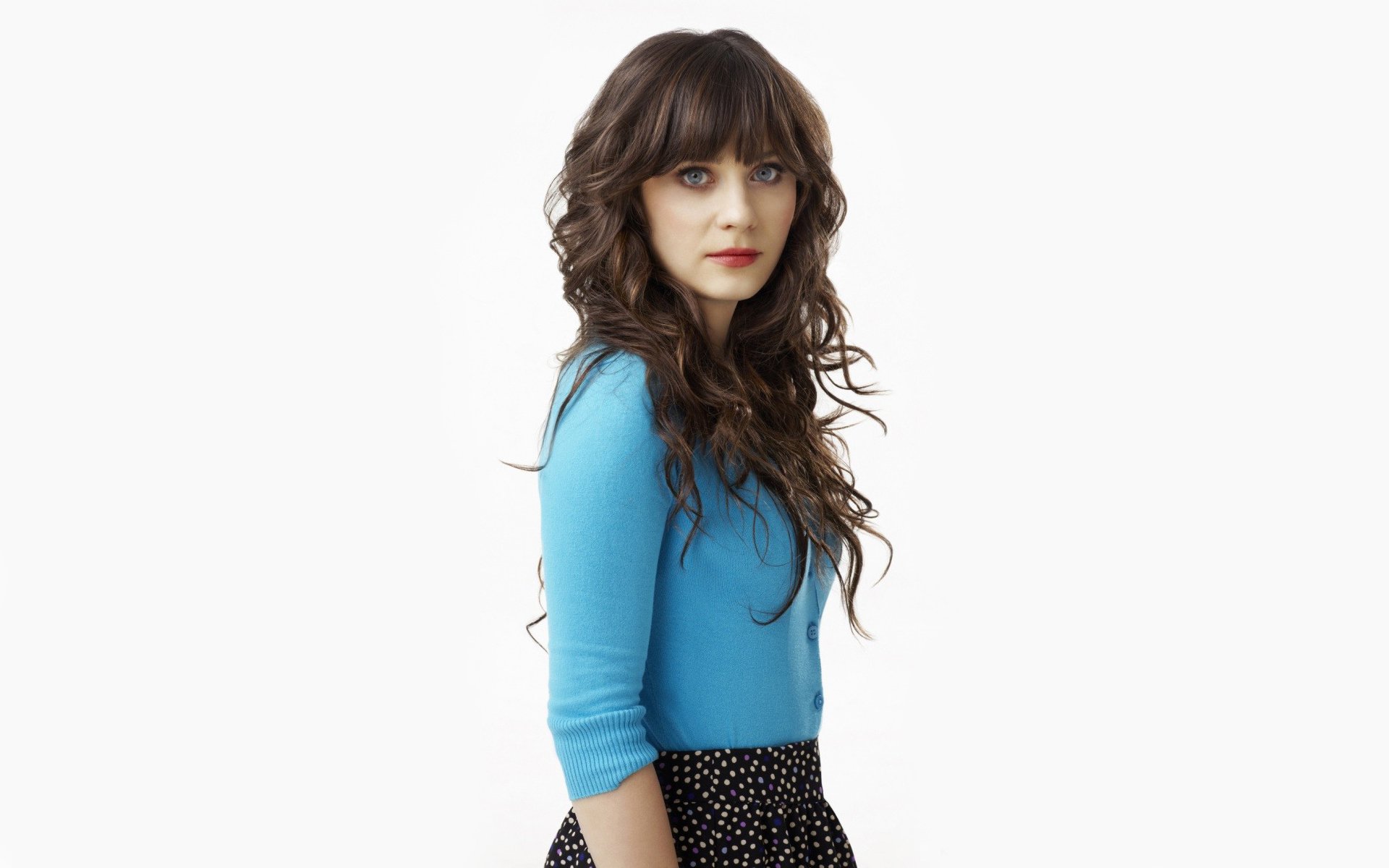 HD PC desktop wallpaper featuring celebrity Zooey Deschanel with long wavy hair, wearing a blue top and black polka dot skirt against a white background.