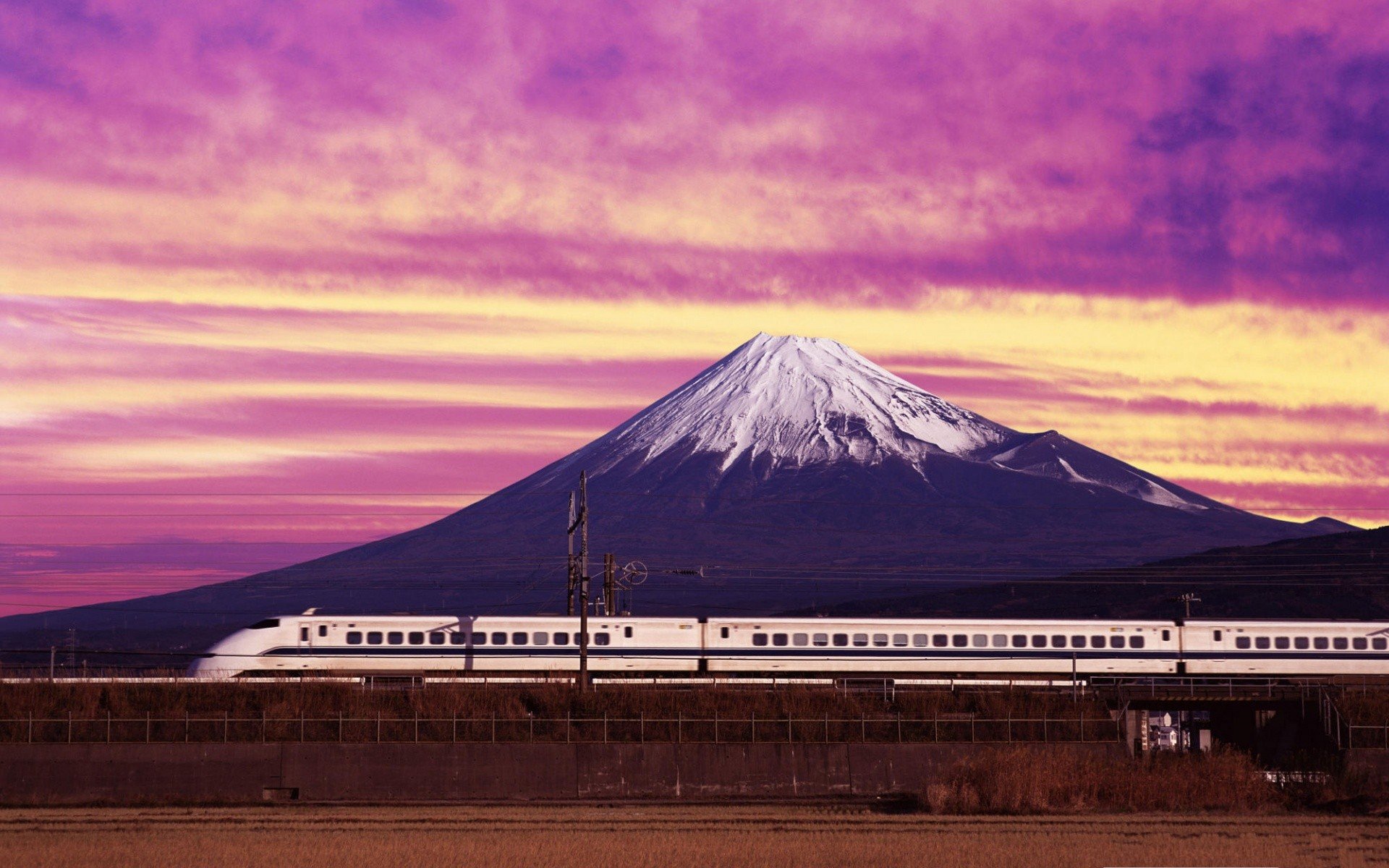 A striking HD image of Mount Fuji at sunset, with vibrant purple skies and a sleek train speeding by, capturing the beauty of Japan's landscape and transportation.