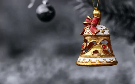 A beautifully decorated gold and white bell ornament, adorned with a red bow, hangs among black Christmas ornaments, creating a festive holiday atmosphere in this HD wallpaper.