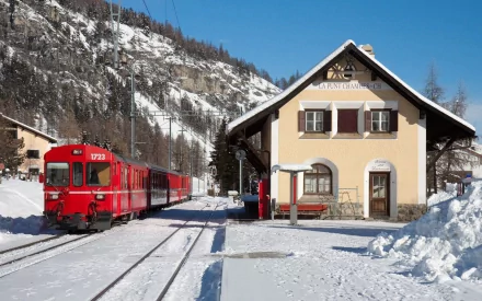 RhB train in Switzerland stopped at a snowy mountain station, captured in a high-definition desktop wallpaper showcasing a bright winter day.