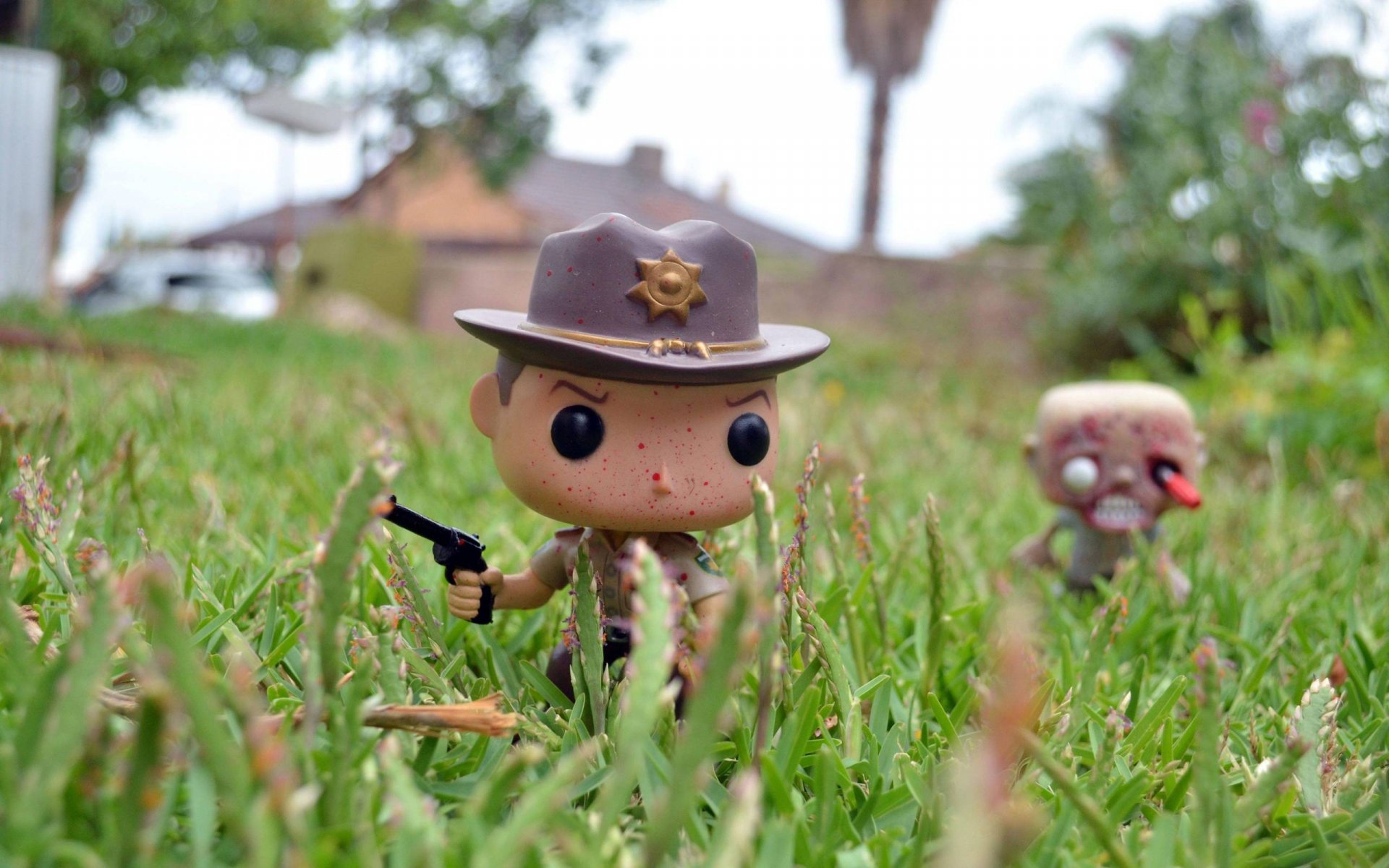 A vibrant HD wallpaper featuring characters from The Walking Dead, with a toy sheriff brandishing a gun in a grassy setting, alongside a quirky zombie figure.