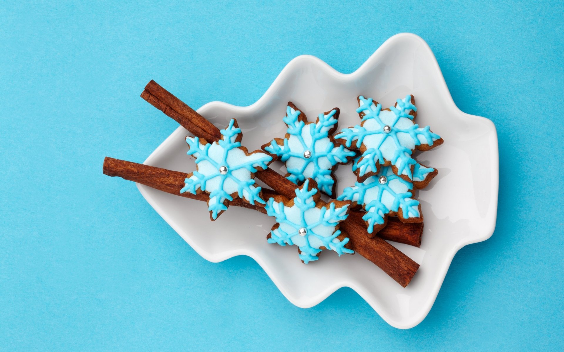 HD desktop wallpaper of blue snowflake-shaped cookies and cinnamon sticks arranged on a white dish, evoking holiday and Christmas vibes.