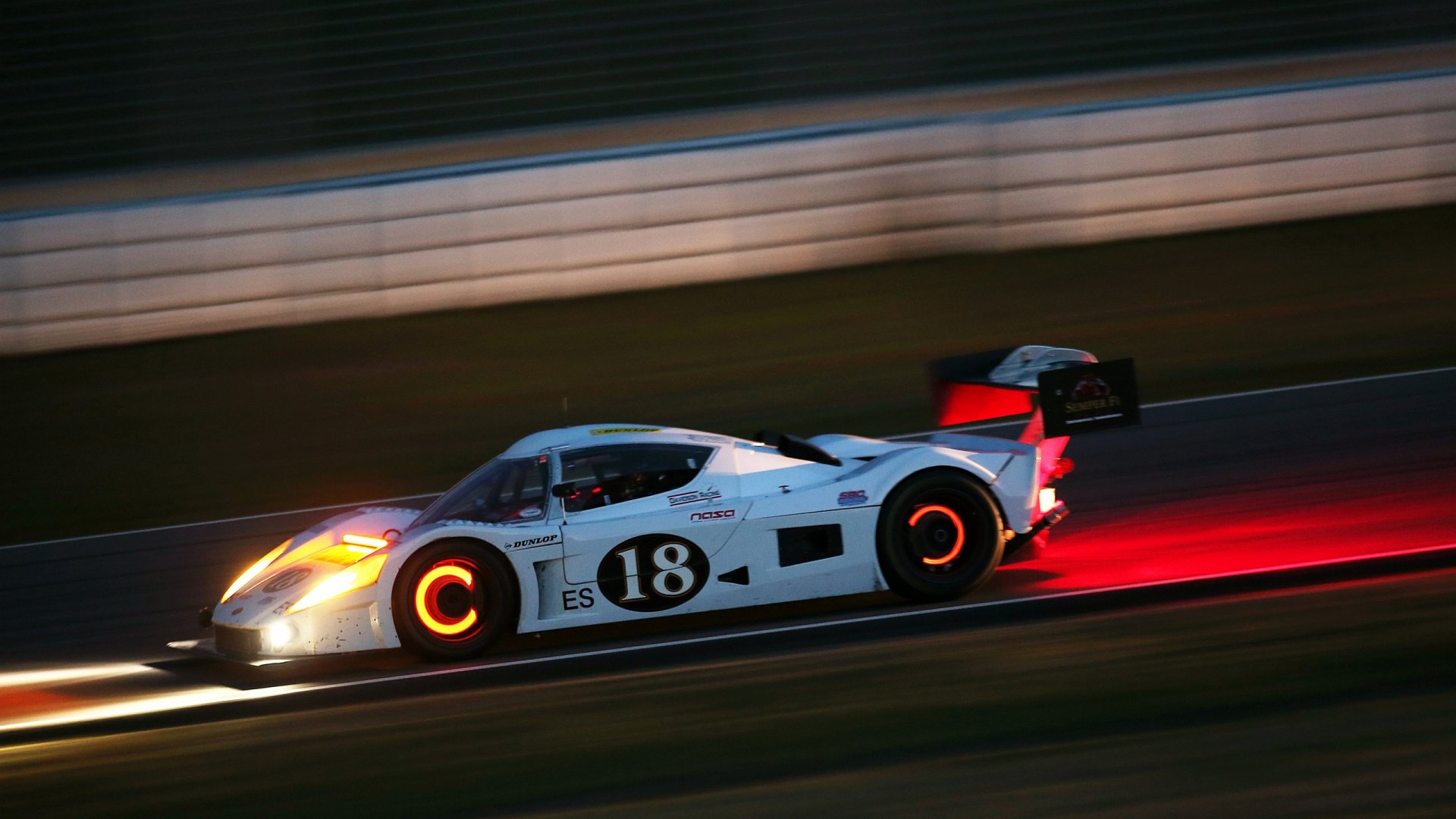 White #18 racing vehicle (car) speeding on a night track with glowing brake discs and red light trails — 2K Quad HD PC desktop wallpaper and background.