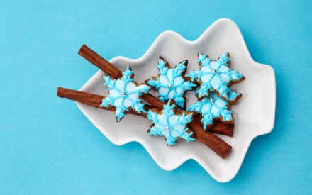 HD desktop wallpaper of blue snowflake-shaped cookies and cinnamon sticks arranged on a white dish, evoking holiday and Christmas vibes.