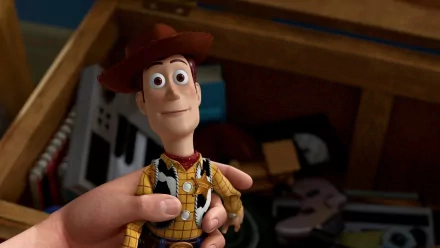A hand holds Woody from Toy Story, captured in an HD desktop wallpaper, showcasing the iconic character against a backdrop of childhood toys.