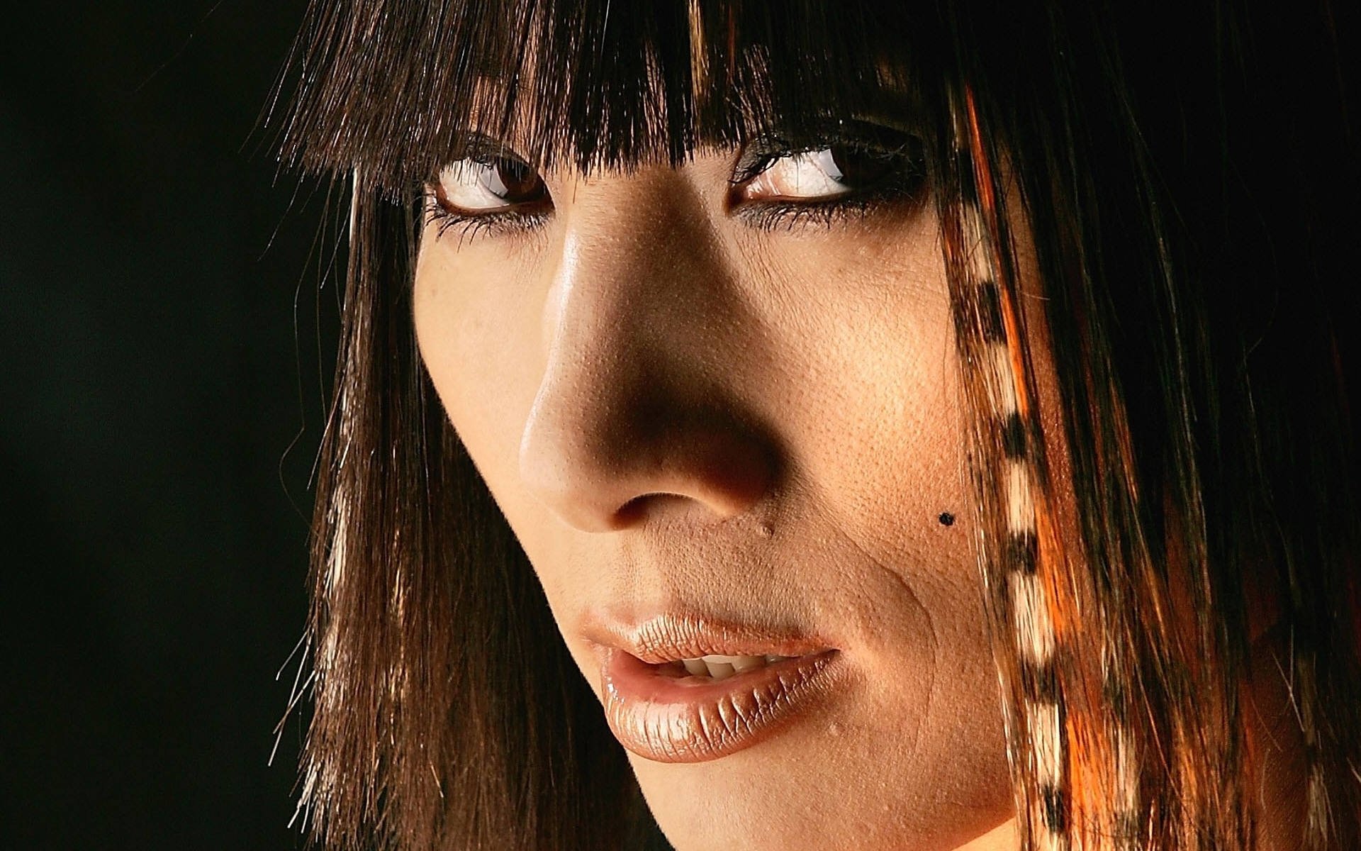 HD PC desktop wallpaper: close-up portrait of a woman's face with dark bangs, smoky eye makeup, and a cheek beauty mark.