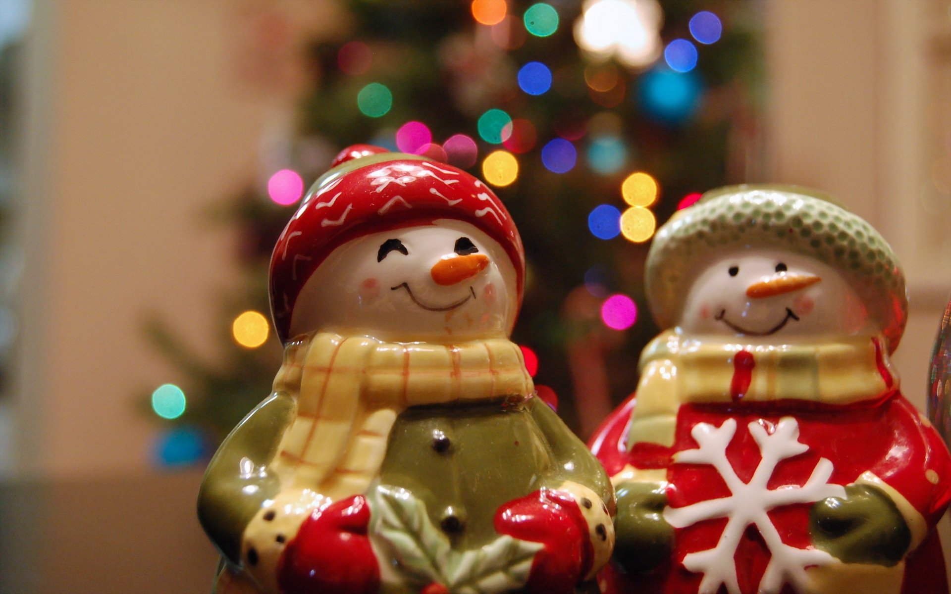 Holiday-themed Christmas wallpaper featuring two smiling snowman figurines against a softly blurred background of colorful holiday lights.