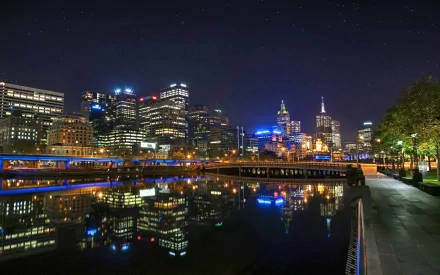 Night view of Melbourne, Australia along the Yarra River: illuminated man-made skyline and riverside walkway reflected on the water — 2K Quad HD PC desktop wallpaper