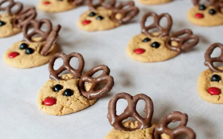 HD desktop wallpaper featuring festive cookies shaped like reindeer faces with pretzel antlers and candy eyes and noses on a white background.