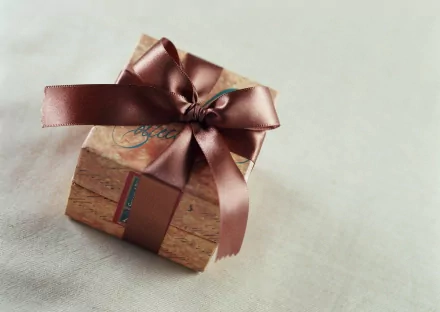 HD PC desktop wallpaper featuring a neatly wrapped wooden gift box tied with a shiny brown ribbon, set against a soft, neutral background.