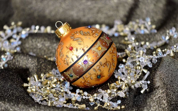 A beautifully decorated golden Christmas ornament rests on sparkling strands, capturing the festive spirit of the holiday season in this vibrant HD desktop wallpaper.