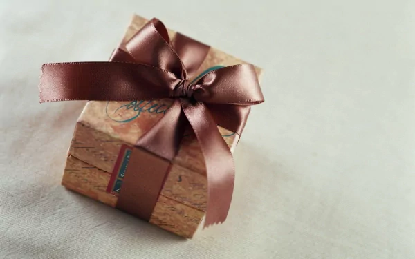 HD PC desktop wallpaper featuring a neatly wrapped wooden gift box tied with a shiny brown ribbon, set against a soft, neutral background.