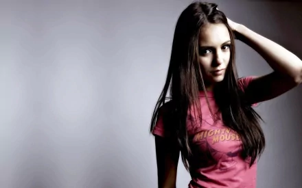 Nina Dobrev poses confidently in a pink t-shirt against a soft gray background, capturing a striking moment for a high-definition desktop wallpaper.