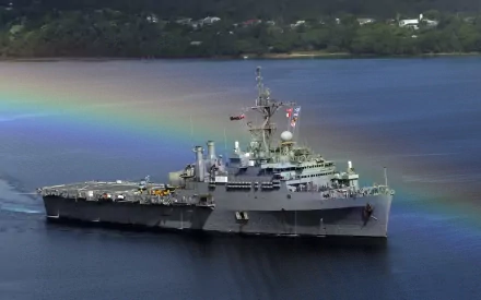 HD desktop wallpaper of the USS Cleveland (LPD-7), a United States Navy amphibious transport dock warship, sailing with a rainbow visible over the water.
