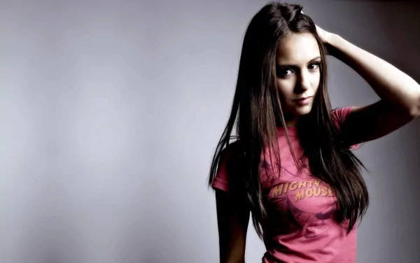 Nina Dobrev poses confidently in a pink t-shirt against a soft gray background, capturing a striking moment for a high-definition desktop wallpaper.