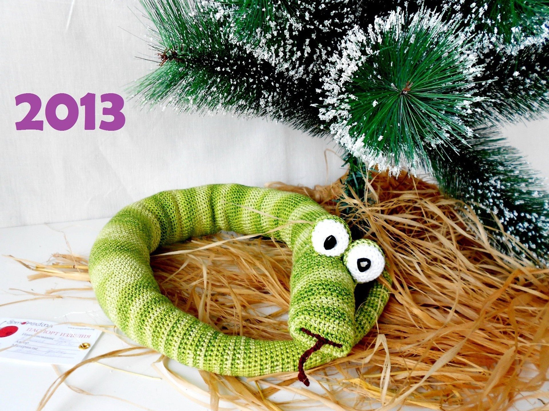 Holiday New Year 2013 HD PC desktop wallpaper/background: knitted green snake with big white eyes curled on straw beneath a snow-dusted pine branch, purple 2013 text.