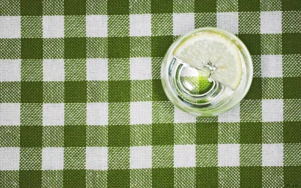 HD desktop wallpaper featuring a top-down view of a glass of lemon water on a green and white checkered tablecloth.