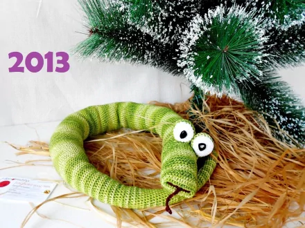 Holiday New Year 2013 HD PC desktop wallpaper/background: knitted green snake with big white eyes curled on straw beneath a snow-dusted pine branch, purple 2013 text.