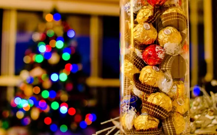 A close-up of a glass jar filled with assorted candies, set against a beautifully lit Christmas tree in the background, creating a festive and inviting atmosphere.
