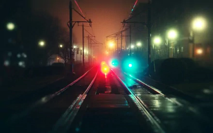 HD wallpaper featuring a misty railroad scene at night with glowing red and blue signal lights along the tracks.