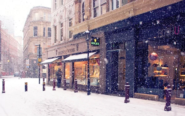 HD desktop wallpaper of a charming winter scene, capturing snow falling gently on a city street lined with shops and old buildings.