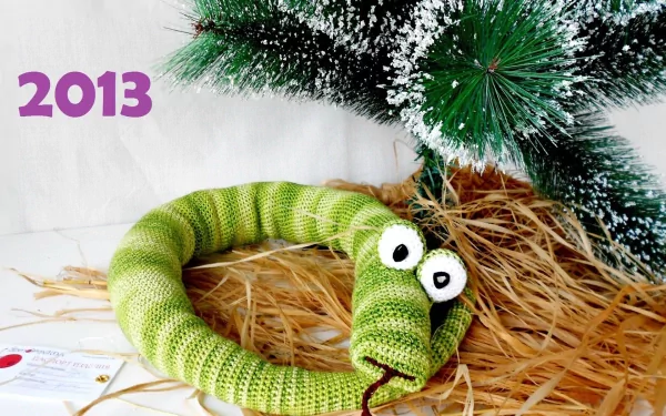 Holiday New Year 2013 HD PC desktop wallpaper/background: knitted green snake with big white eyes curled on straw beneath a snow-dusted pine branch, purple 2013 text.