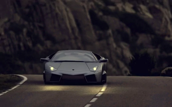 HD wallpaper of a Lamborghini Reventón driving on a mountain road at dusk.