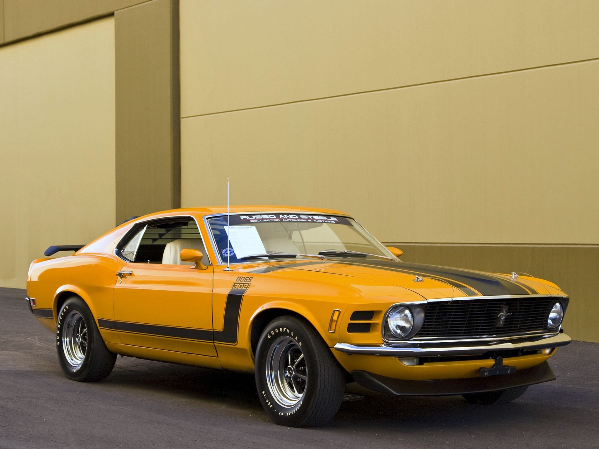 HD desktop wallpaper featuring a vibrant yellow Ford Mustang Boss 302 fastback muscle car parked against a minimalist beige wall background.